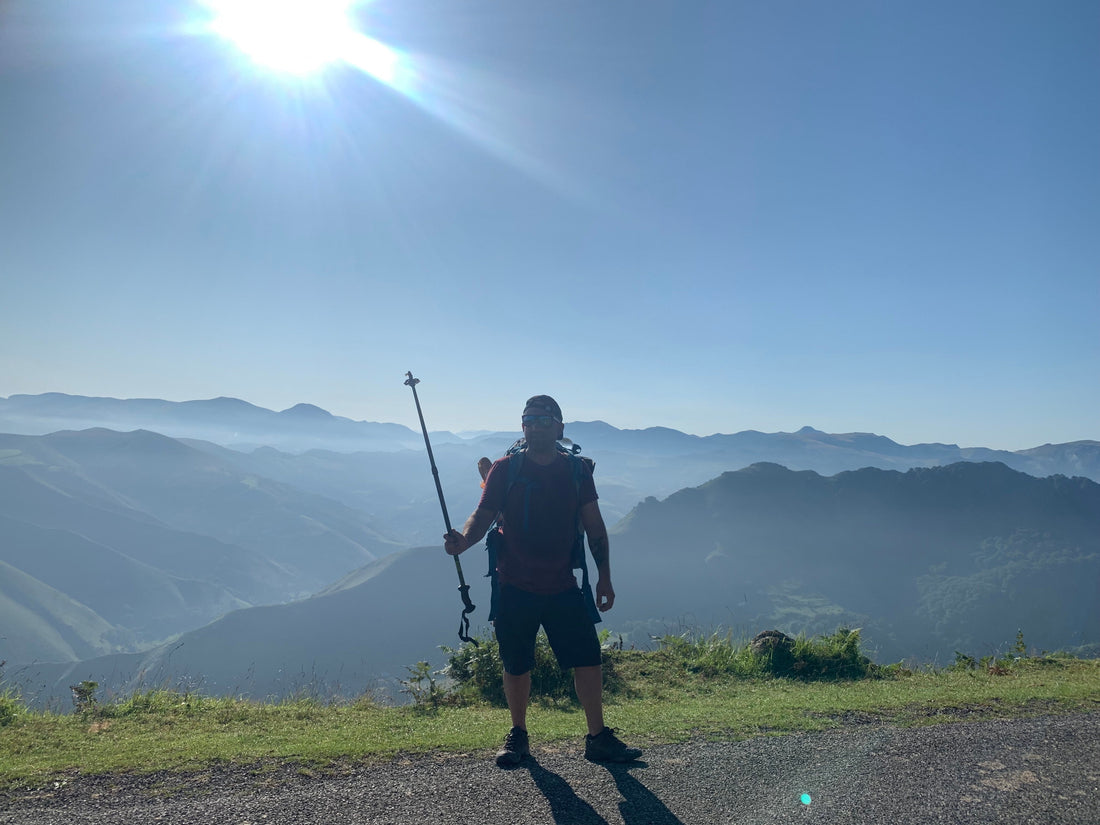 Pellegrino in controluce con il bastoncino alzato sulle montagne del Cammino