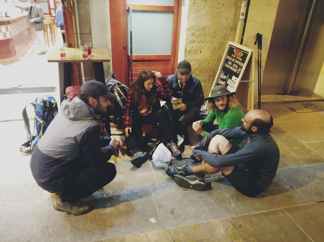 Gruppo di pellegrini in pausa sotto un portico durante una tappa del Cammino
