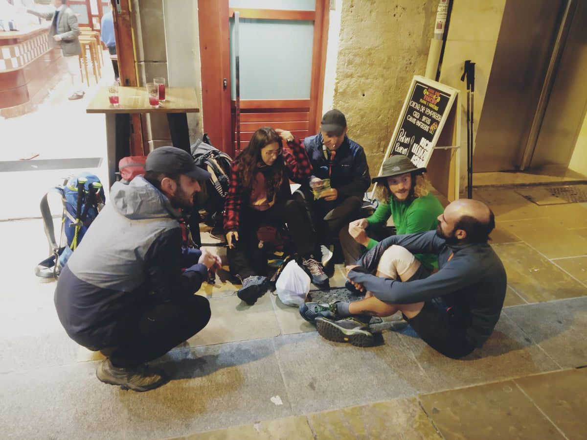 Gruppo di pellegrini in pausa sotto un portico durante una tappa del Cammino