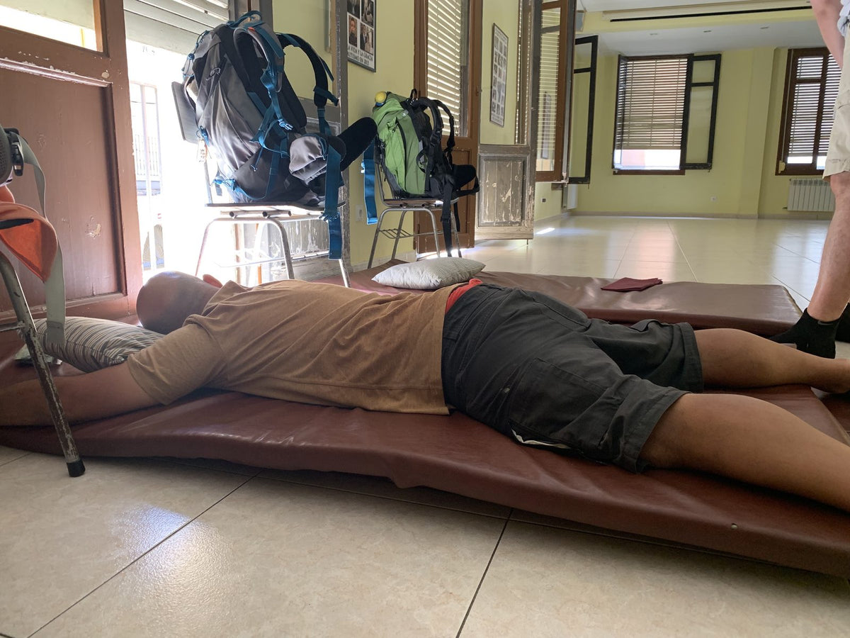 Un pellegrino dorme su un materasso appoggiato per terra nella sala di un albergue del Cammino di Santiago