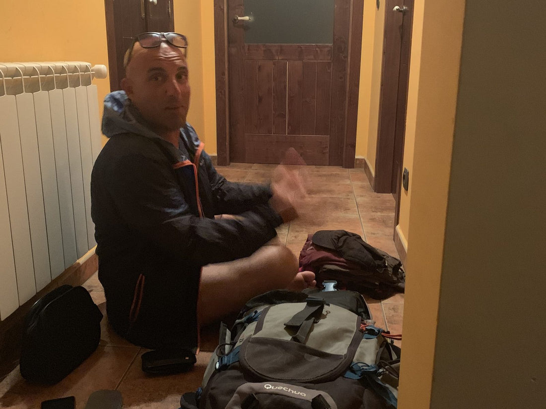 Pellegrino seduto per terra nel corridoio di un albergue con lo zaino aperto, sul Cammino di Santiago