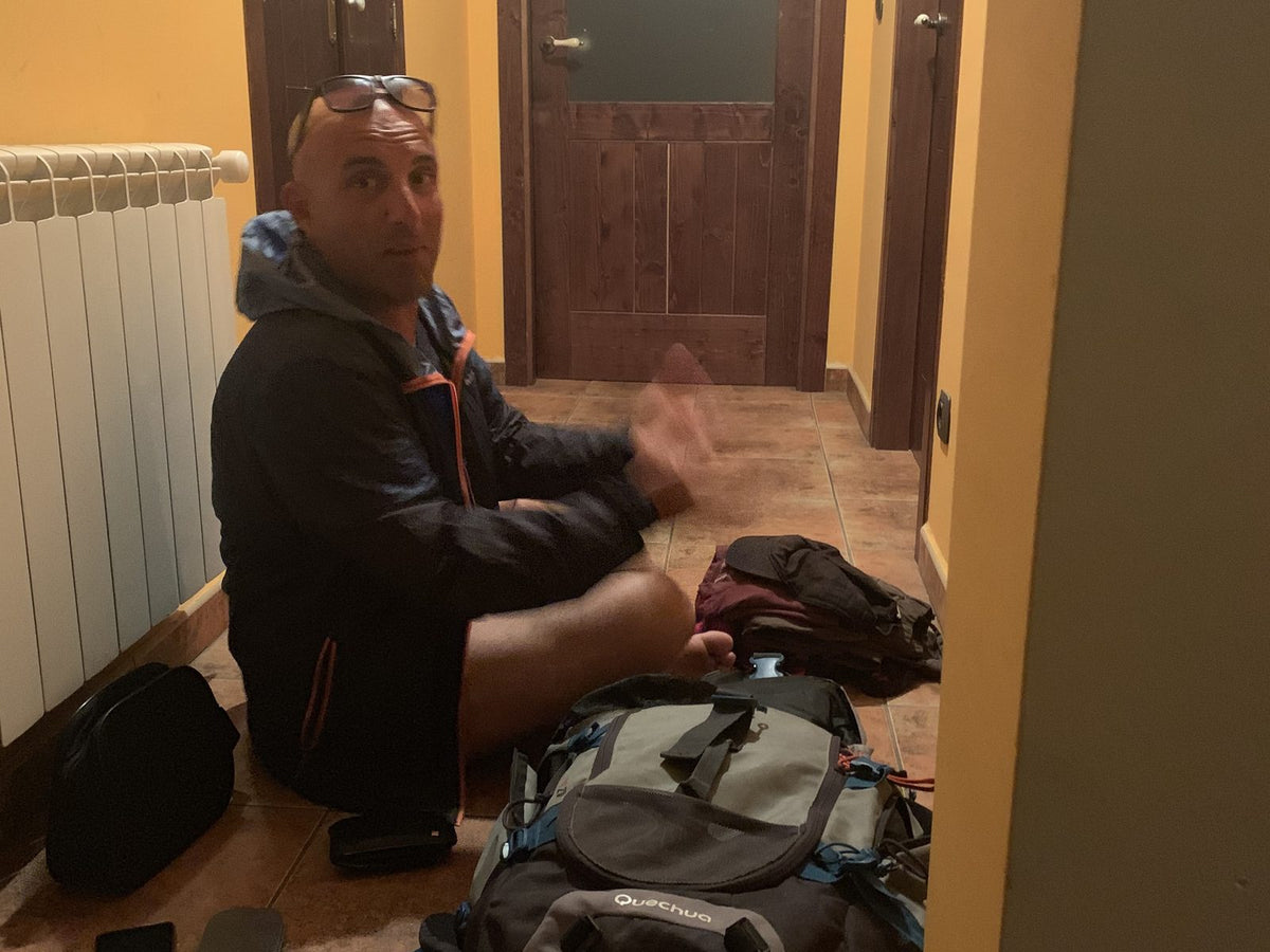 Pellegrino seduto per terra nel corridoio di un albergue con lo zaino aperto, sul Cammino di Santiago